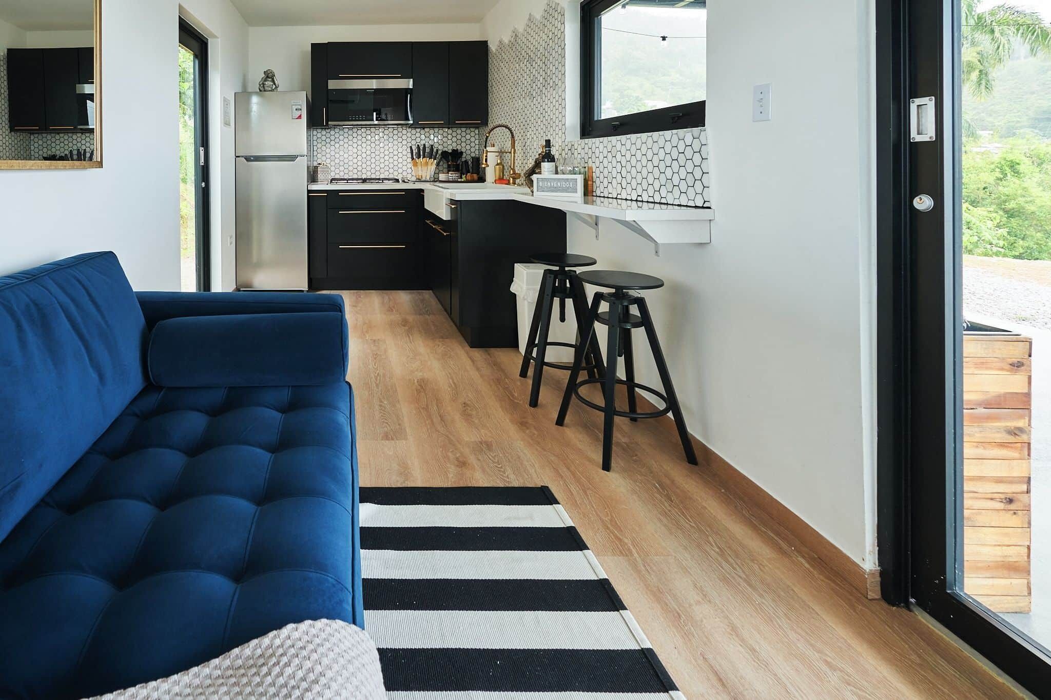 Un espacio habitable compacto con sofá, zona de cocina y vista a través de un ventanal.