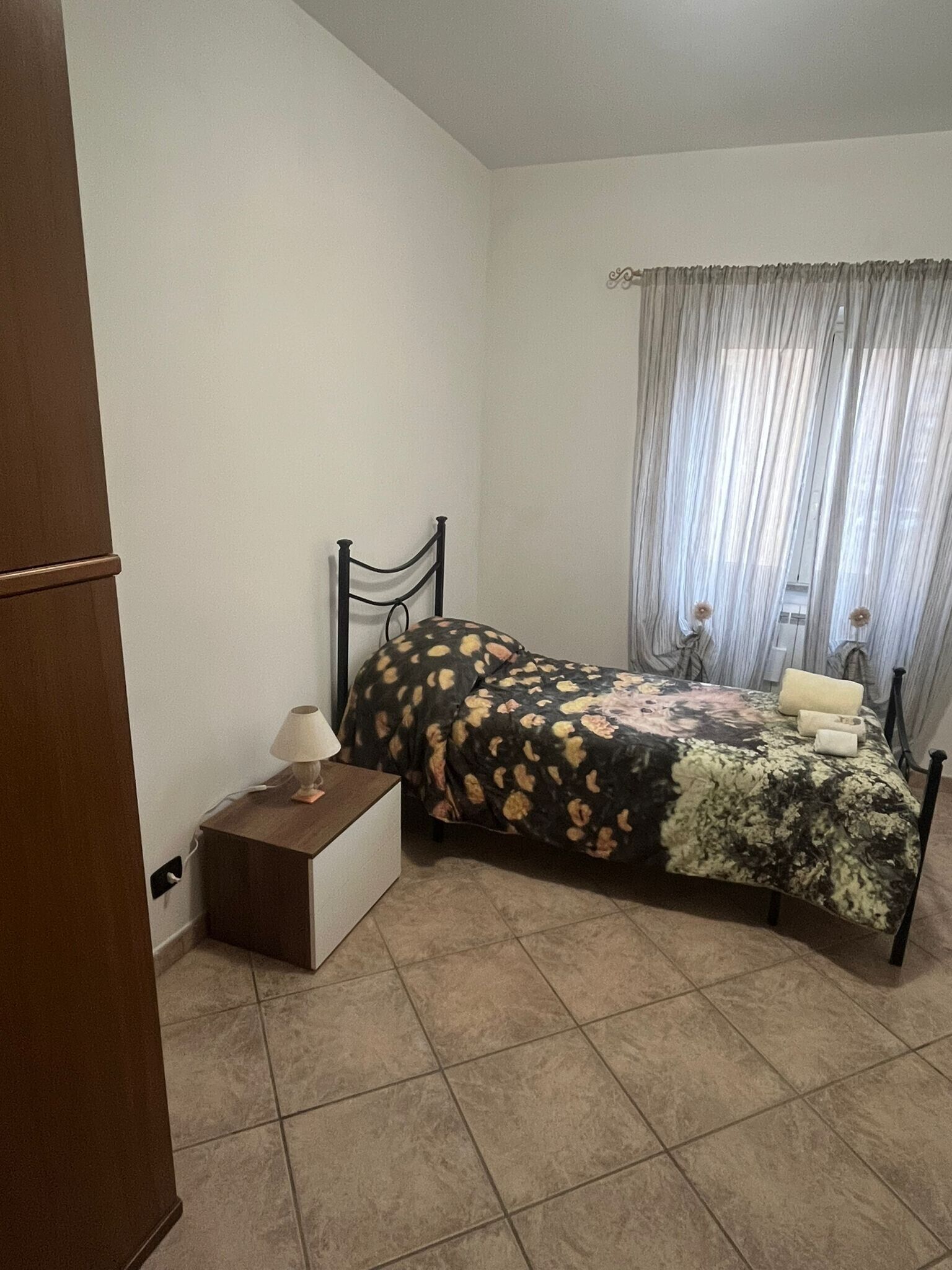 Une chambre à coucher avec un lit, une table de chevet, une lampe et une fenêtre avec des rideaux.