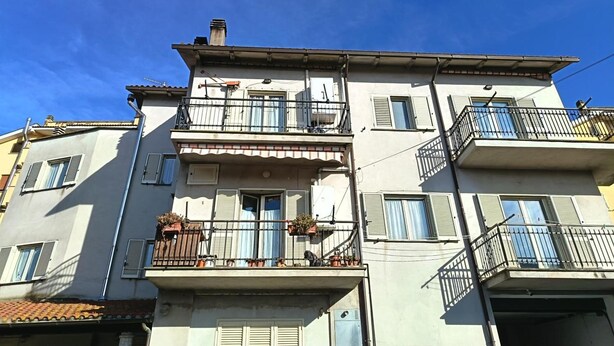 Un immeuble à plusieurs étages, doté de balcons et de fenêtres avec volets, se dressant sous un ciel d’un bleu limpide.