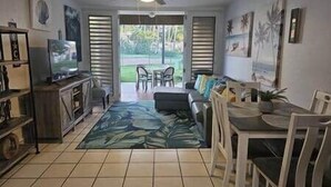 Una sala de estar con televisor, un sofá, una mesa de comedor con sillas y un ventilador de techo.