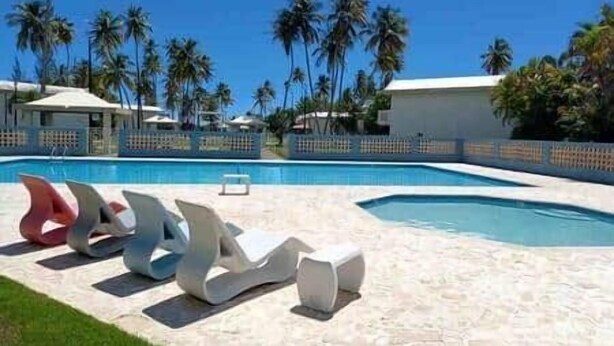 Una piscina con sillones de descanso y palmeras al fondo.