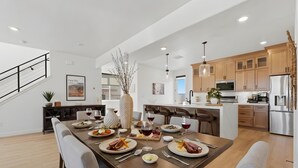A modern kitchen with wooden cabinets, stainless steel appliances, and a dining area with a long table set for a meal. - Lake and Lift Lodge at Gondola Crossing (Heber City)