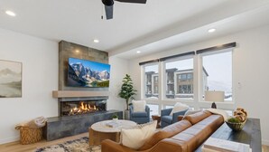 A modern living room with a fireplace, comfortable seating, a television, and large windows. - Lake and Lift Lodge at Gondola Crossing (Heber City)