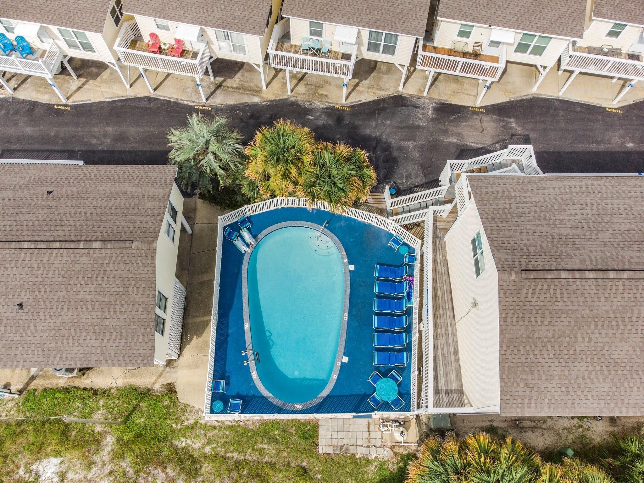 Vue aérienne d’un complexe hôtelier doté d’une grande piscine, entourée de chaises longues et d’une terrasse couverte.