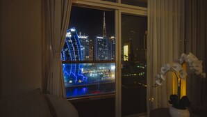A room with a large window overlooking a cityscape at night, featuring illuminated buildings and a view of the water. - Waterfront Escape | Burj & Canal View | Pool+Sauna (Dubai)