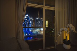 A room with a large window overlooking a cityscape at night, featuring illuminated buildings and a view of the water. - Waterfront Escape | Burj & Canal View | Pool+Sauna (Dubai)