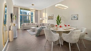 A modern living room with a sectional sofa, a round dining table with six chairs, and a large window offering a city view. - Waterfront Escape | Burj & Canal View | Pool+Sauna (Dubai)