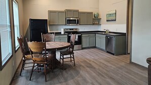 Cozinha moderna com área de jantar, apresentando uma mesa redonda e cadeiras de madeira, geladeira, micro-ondas, forno e lava-louças.
