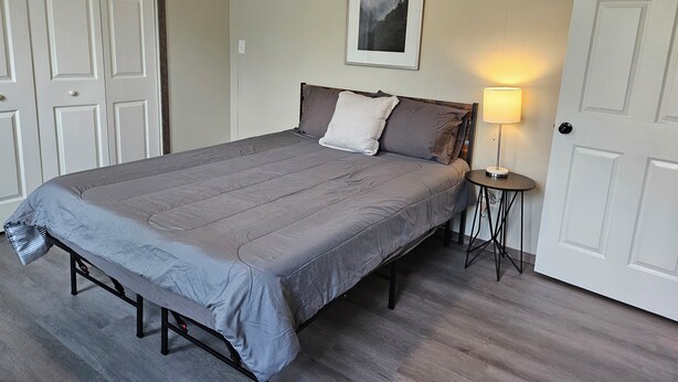 Quarto com cama, mesa de cabeceira com abajur e quadro na parede.