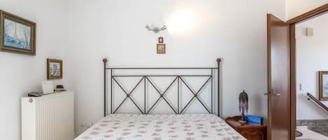 A bedroom with a bed, radiator, framed pictures, and a door leading to another room.