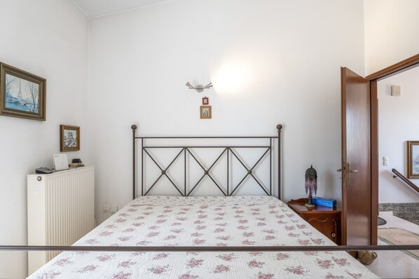 Een slaapkamer met een bed, een radiator, ingelijste foto's en een deur naar een andere kamer.