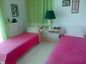 Ein Zimmer mit zwei Betten, einem Schreibtisch, einer Lampe und einem Fenster mit grünen Vorhängen.
