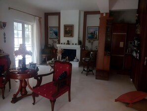 A living room with a fireplace, a dining area with a table and chairs, and a kitchen area with cabinets and a refrigerator.