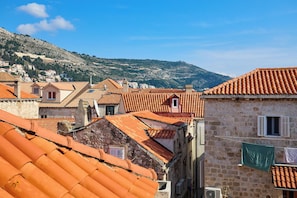 A view of terracotta-roofed buildings with stone walls, a hillside in the background, and a clear blue sky. - Sophie 1 - Old Town Heritage Suite (Dubrovnik)