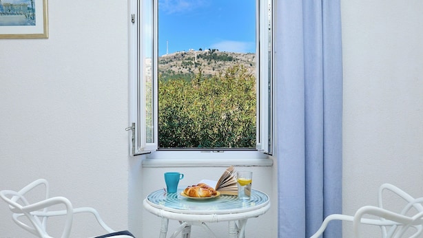 A room with a view of a hill, a table with a book, a glass of juice, and two chairs. - Sophie 1 - Old Town Heritage Suite (Dubrovnik)