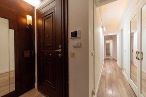 Un couloir avec une porte en bois, un luminaire fixé au mur et un thermostat.