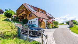 Een huis met een auto voor de deur, een verharde oprit en een houten hek.