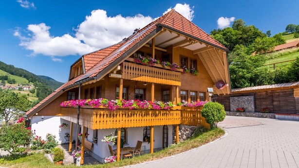 Een traditioneel houten huis met een balkon, een veranda en een verharde oprit.