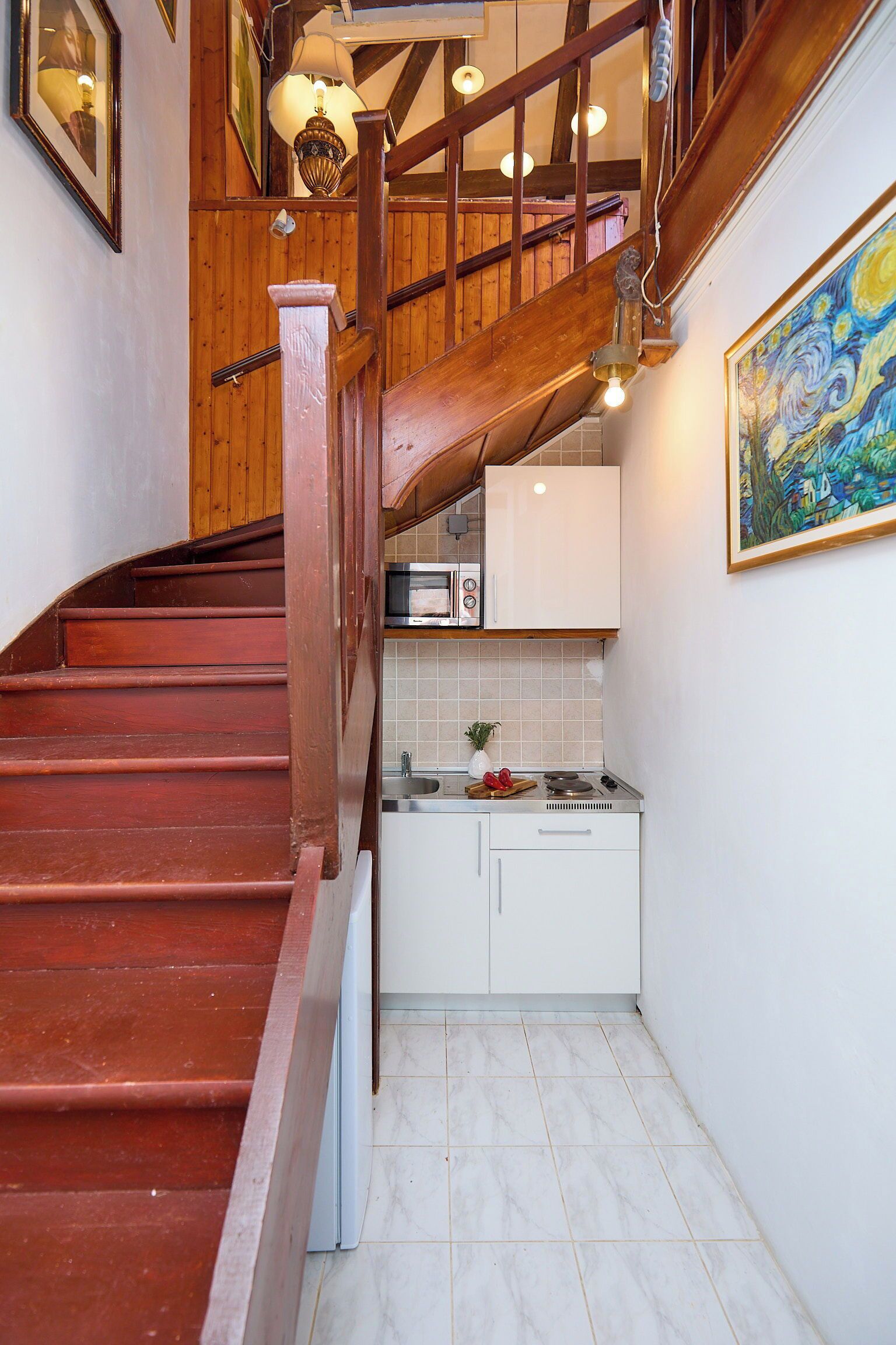 Eine Treppe führt zu einer Küche mit weißen Schränken, einer Mikrowelle und einem Bild an der Wand.