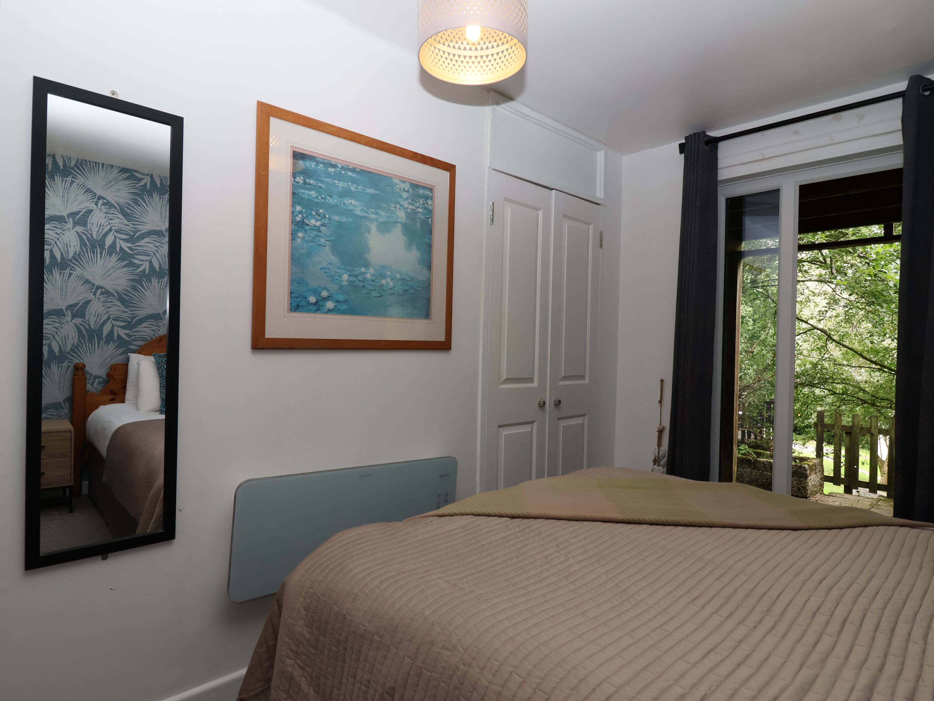 Ein Schlafzimmer mit einem Bett, einem gerahmten Gemälde, einem Spiegel und einer Tür, die auf einen Balkon führt.