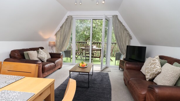 A spacious living room with a brown leather sofa, a wooden coffee table, and a TV on a wooden stand.