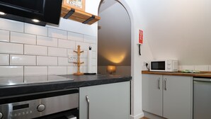 A modern kitchen with white cabinets, a black countertop, stainless steel appliances, and a wooden hanging rack.