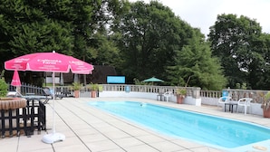 An outdoor swimming pool with lounge chairs and umbrellas, surrounded by a fence and trees.