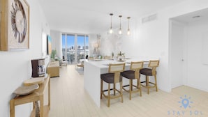 A modern kitchen with a central island, bar stools, and a large clock on the wall. - Stunning 1BR Apartment with Balcony & Pool (Hallandale Beach)