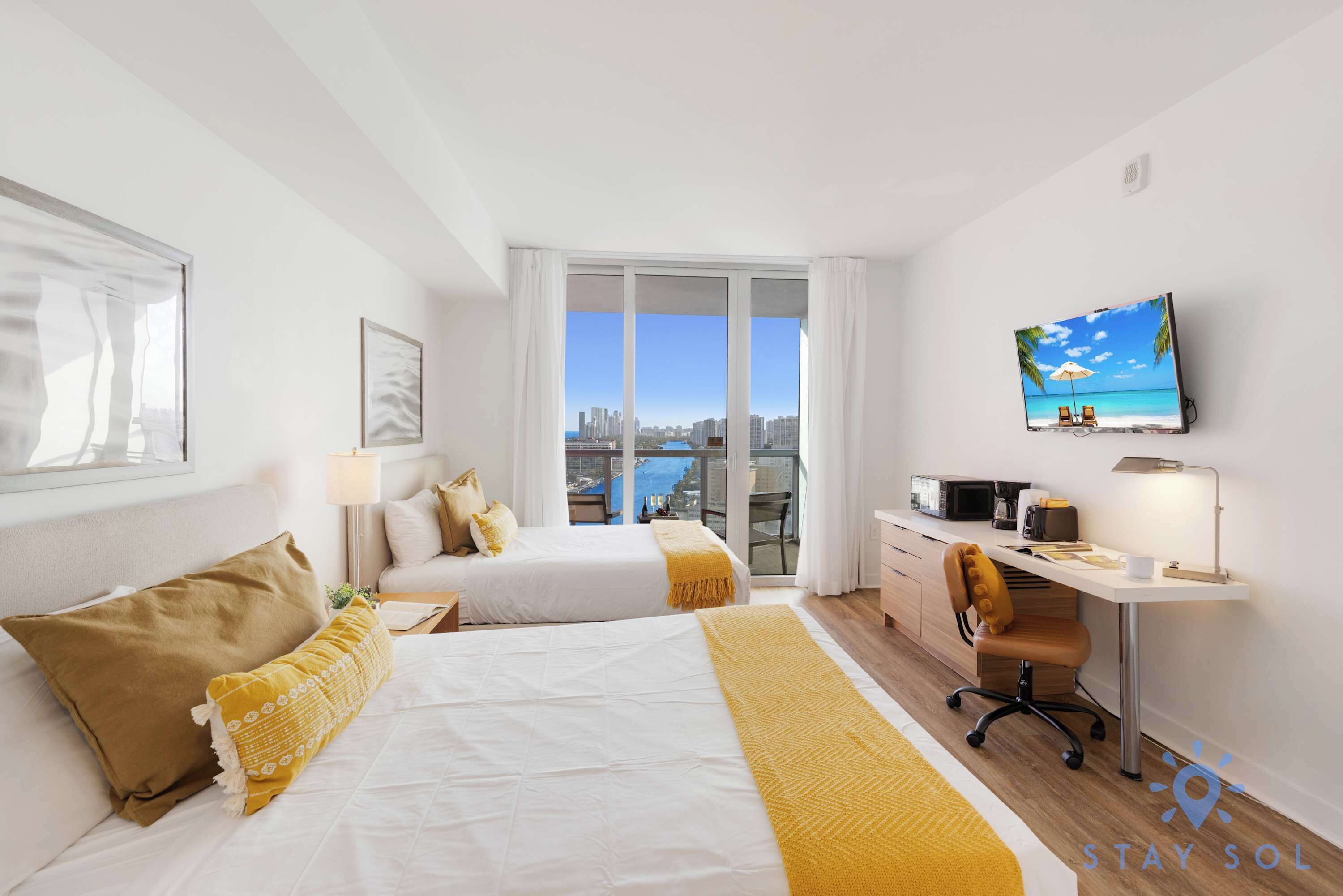 Habitació d'hotel amb dos llits, una taula de treball, televisió i vista a la ciutat.