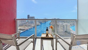 A balcony with a table, two chairs, a bottle of wine, and a vase with flowers. - Beautiful Studio w/ Stunning Views + pool + gym (Hallandale Beach)