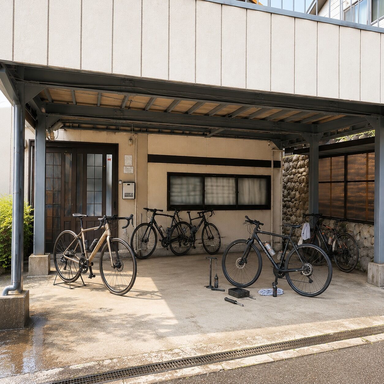 A covered bike parking area with bicycles, a door, and a stone wall.