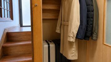 Una escalera de madera que conduce a una habitación con un perchero que sostiene varias chaquetas y una maleta.