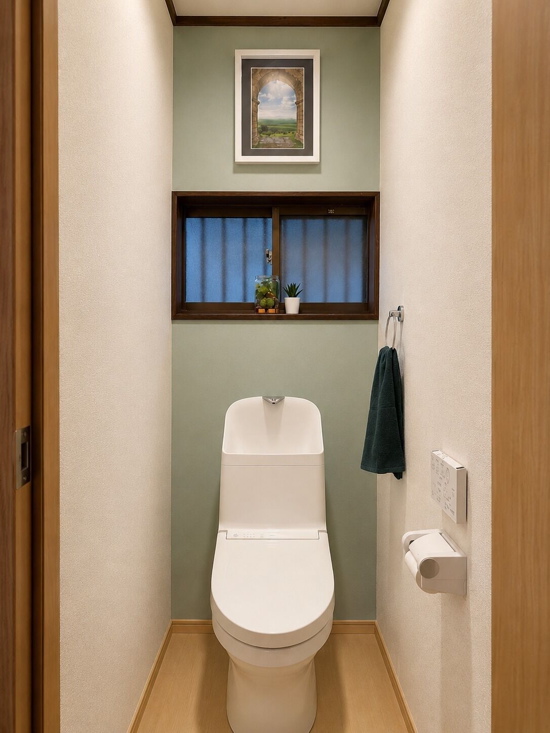 A small bathroom with a toilet, a window with curtains, a framed picture on the wall, and a towel rack.