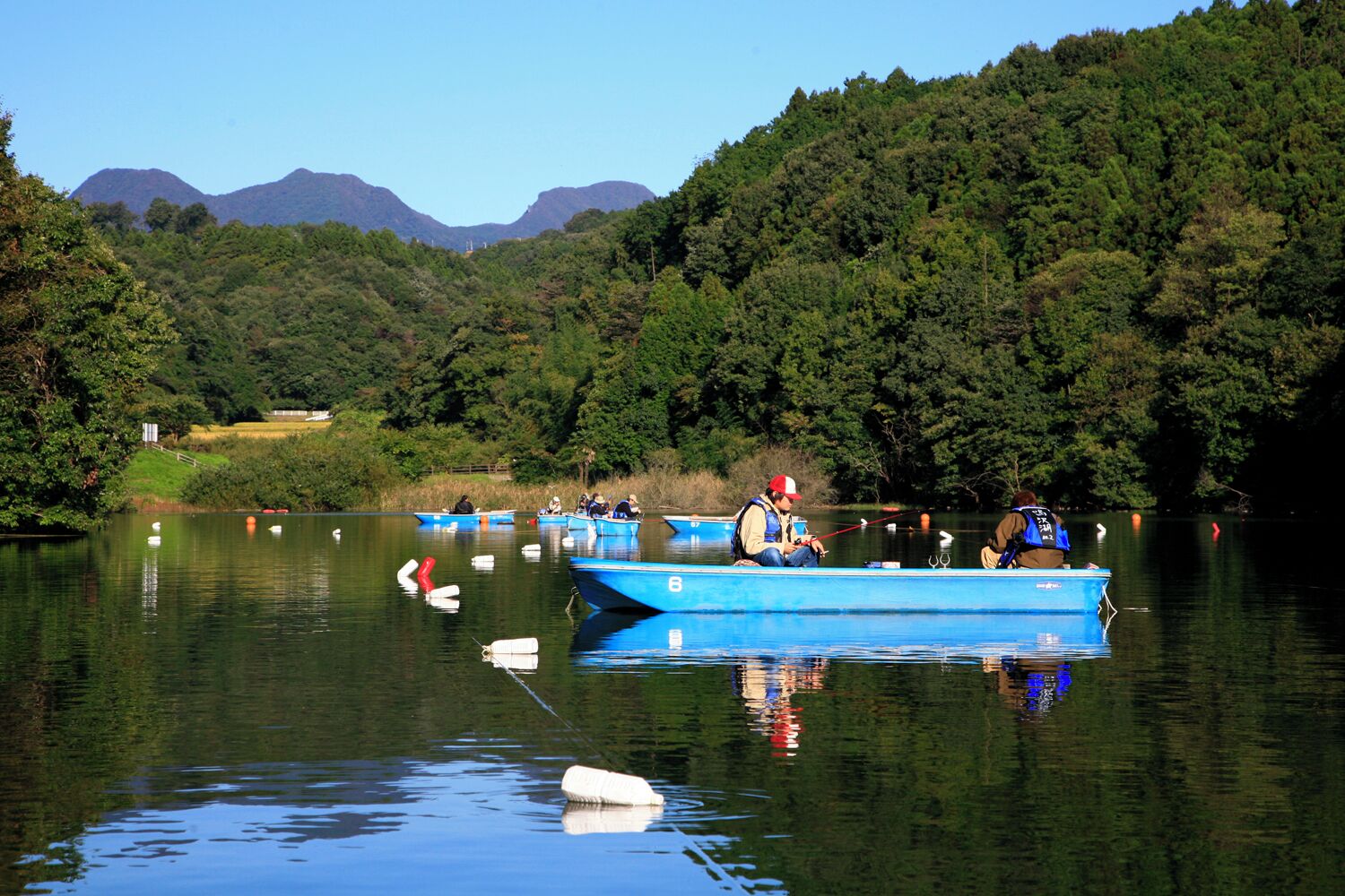 A calm lake with several small boats, surrounded by dense forest and distant mountains.