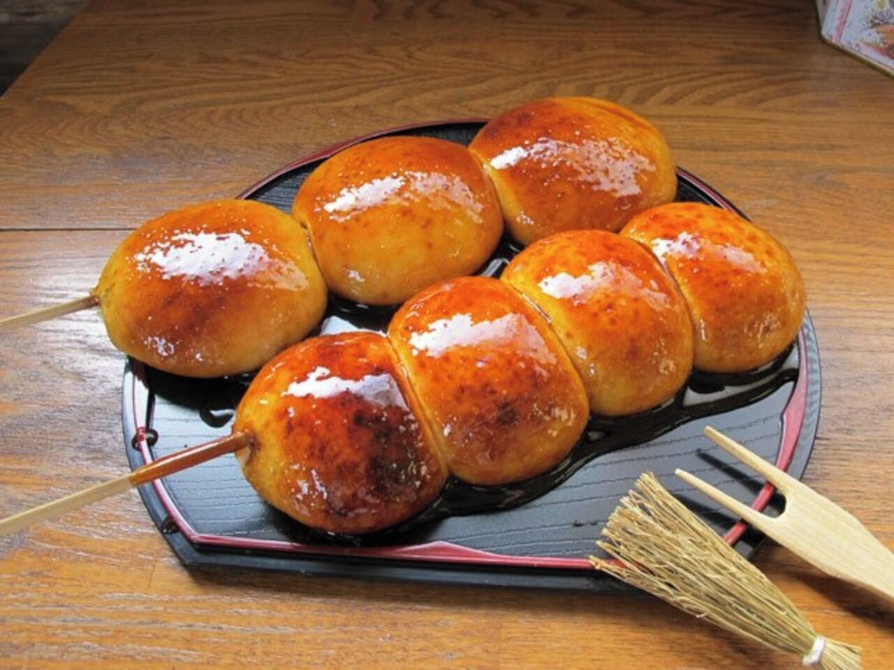 A plate of glazed buns on a dark plate with a wooden fork beside it.