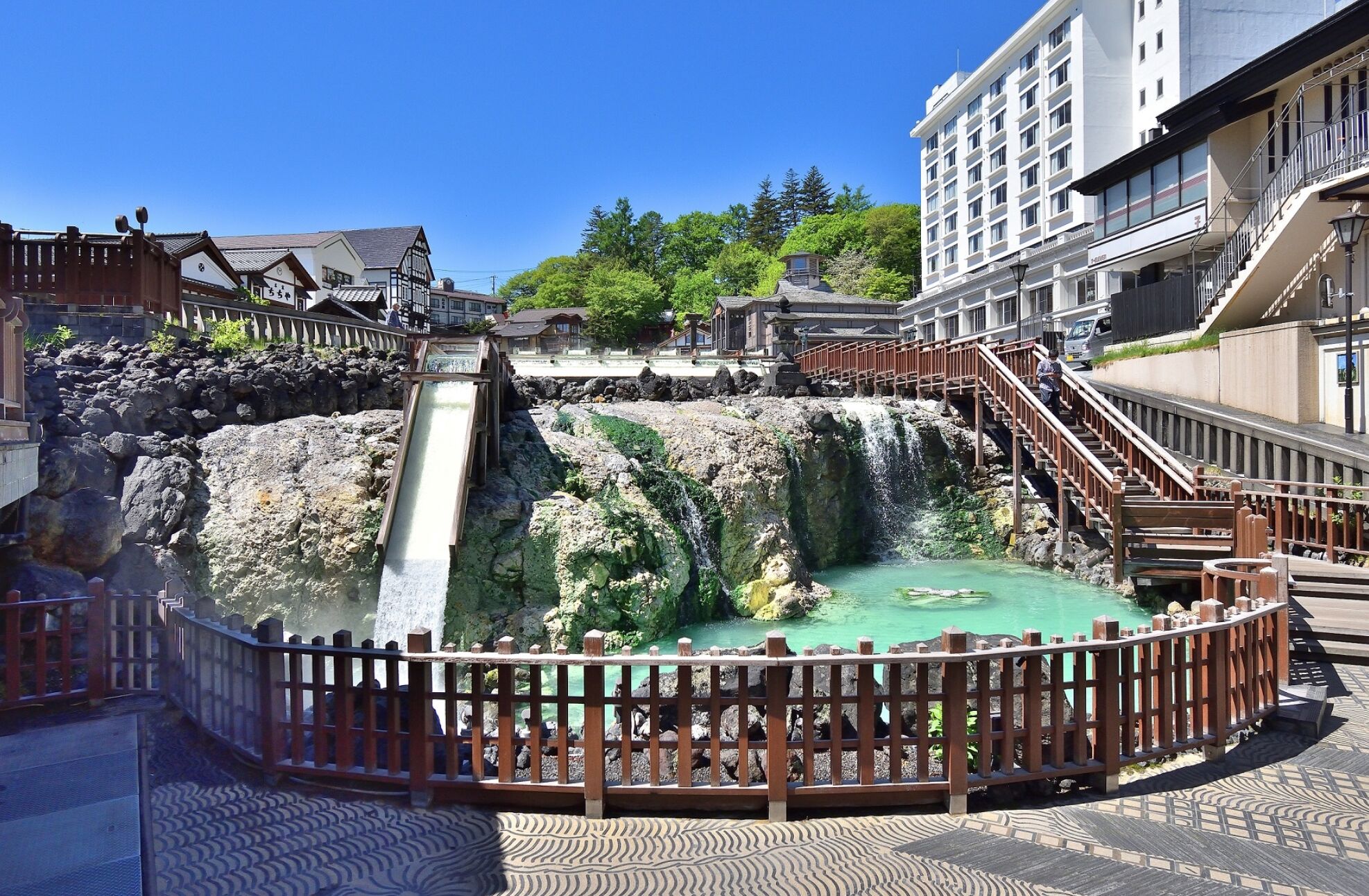 A traditional Japanese onsen with a wooden walkway and a stone waterfall.