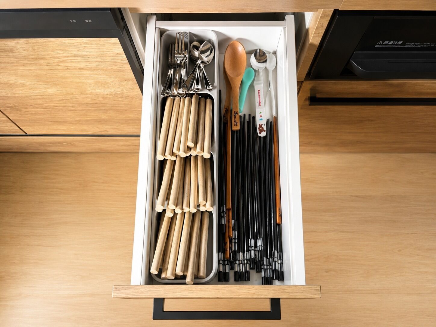 A drawer with utensils, chopsticks, and a spoon.