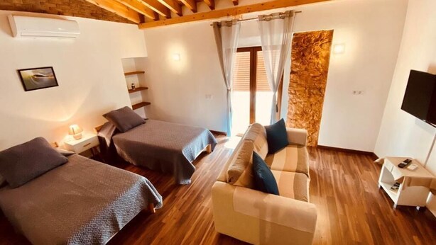 A room with two beds, a sofa, a TV, and a stone accent wall. - AlvorKiteCenter Guesthouse (Portimao)