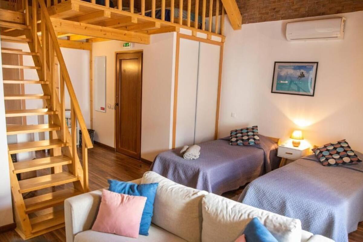 Ein Zimmer mit zwei Betten, einer Holztreppe, einer Couch und einer Wand-Klimaanlage.