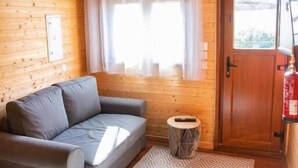 A cozy log cabin room with a gray sofa, a patterned rug, a small round table, and a wooden door. - AlvorKiteCenter Guesthouse (Portimao)
