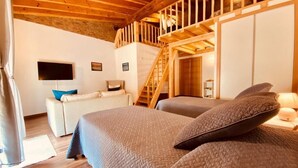 A bedroom with a wooden ceiling, a staircase, a bed with a quilted cover, a sofa, and a flat-screen TV. - AlvorKiteCenter Guesthouse (Portimao)