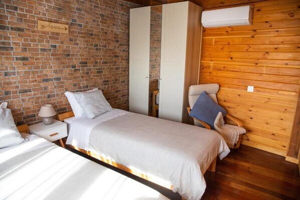 Une chambre avec un mur en briques, un lambris en bois, un lit avec une literie blanche, une table de chevet avec une lampe et une armoire.
