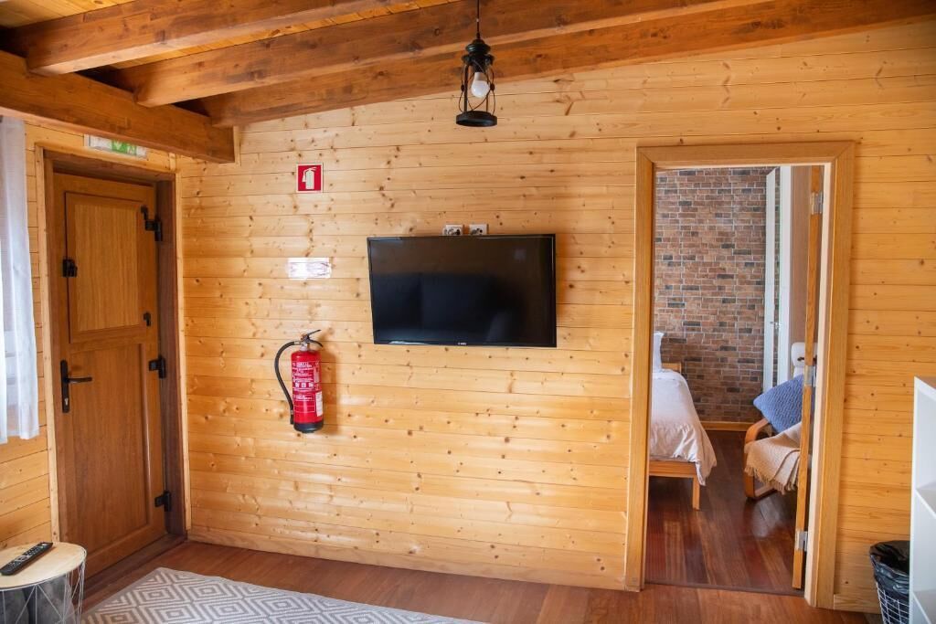A wooden-paneled room with a television mounted on the wall, a fire extinguisher, and a door leading to another room.