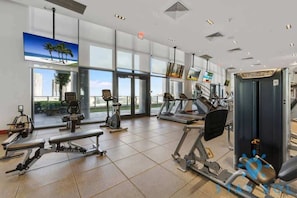 A modern gym with various exercise equipment, large windows, and a view of the cityscape. - Modern Stylish 1BR Apartment (Miami)