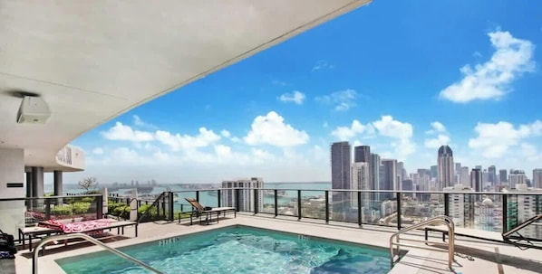 A rooftop pool with a city skyline view, lounge chairs, and a glass railing. - Modern Stylish 1BR Apartment (Miami)