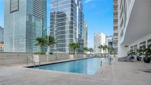 A swimming pool with a concrete deck, surrounded by palm trees and modern buildings. - Comfortable Apartment with pool (Miami)