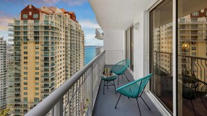 A balcony with a table and chairs, overlooking a high-rise building and the sea. - Comfortable Apartment with pool (Miami)