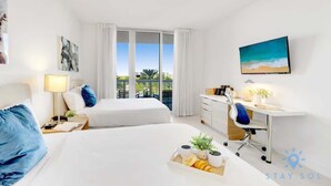 Een hotelkamer met twee bedden, een bureau met stoel, een groot raam met gordijnen en een schilderij aan de muur.