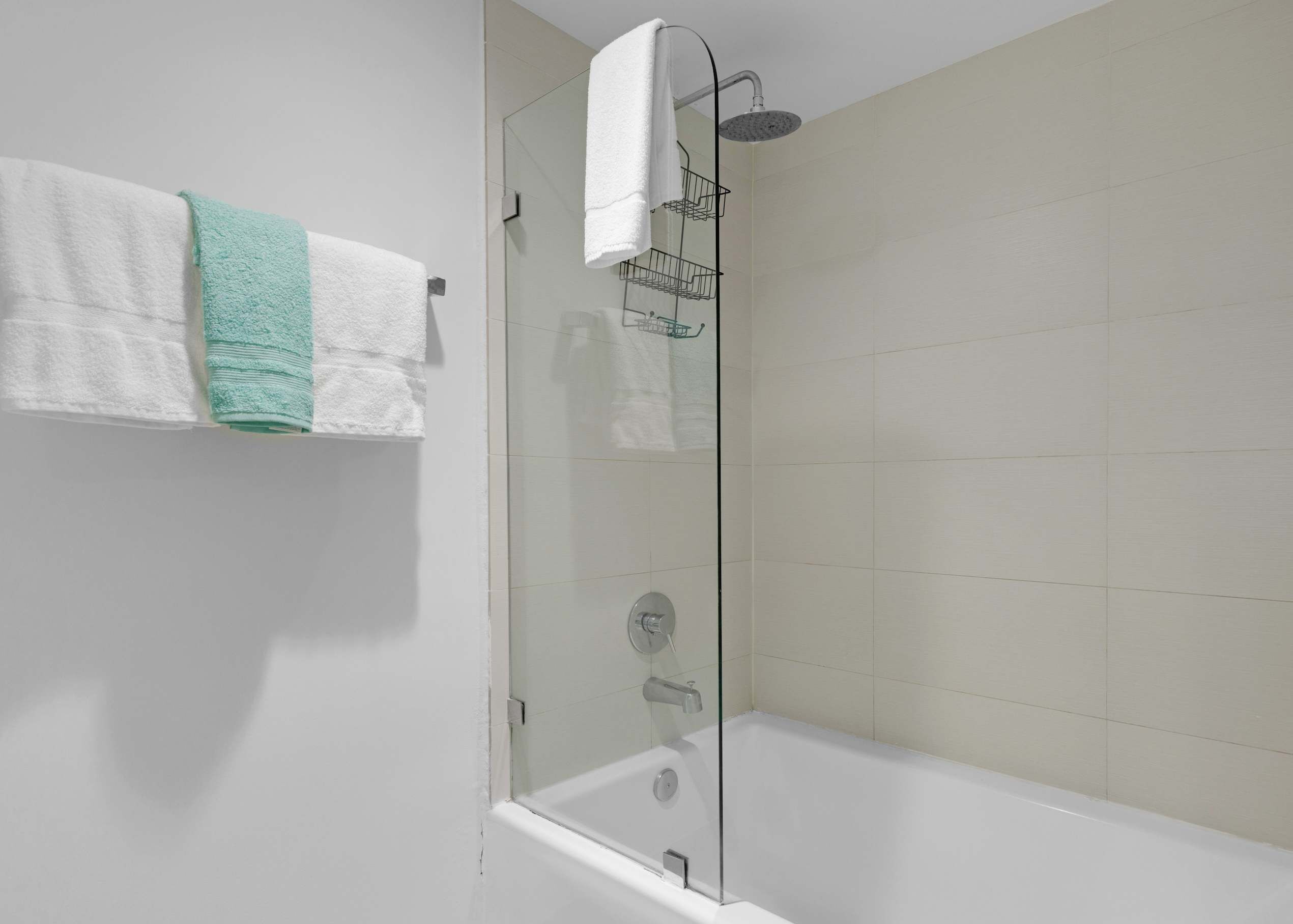A modern bathroom with a glass-enclosed shower, a white bathtub, and a towel rack with two towels.
