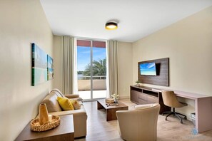 A modern hotel room with a sofa, a desk, a television, and a large window with a view of palm trees. - Beautiful 2BR Apt w/ Amazing Pool+ Hot Tub (Hollywood)